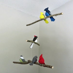 May include: A mobile with five felt birds hanging from branches. The birds are yellow, blue, black and white, gray, and red.