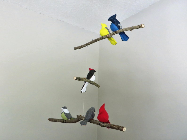 May include: A mobile with five felt birds hanging from branches. The birds are yellow, blue, black and white, gray, and red.