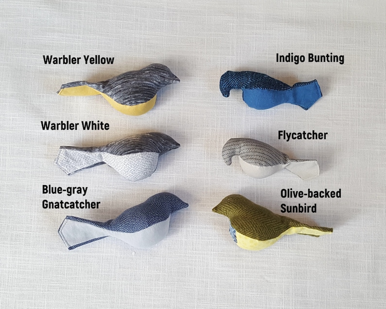May include: Six handmade fabric bird toys in various colors and patterns, including yellow, white, blue, gray, and green. The birds are labeled with their names: Warbler Yellow, Indigo Bunting, Warbler White, Flycatcher, Blue-gray Gnatcatcher, and Olive-backed Sunbird.