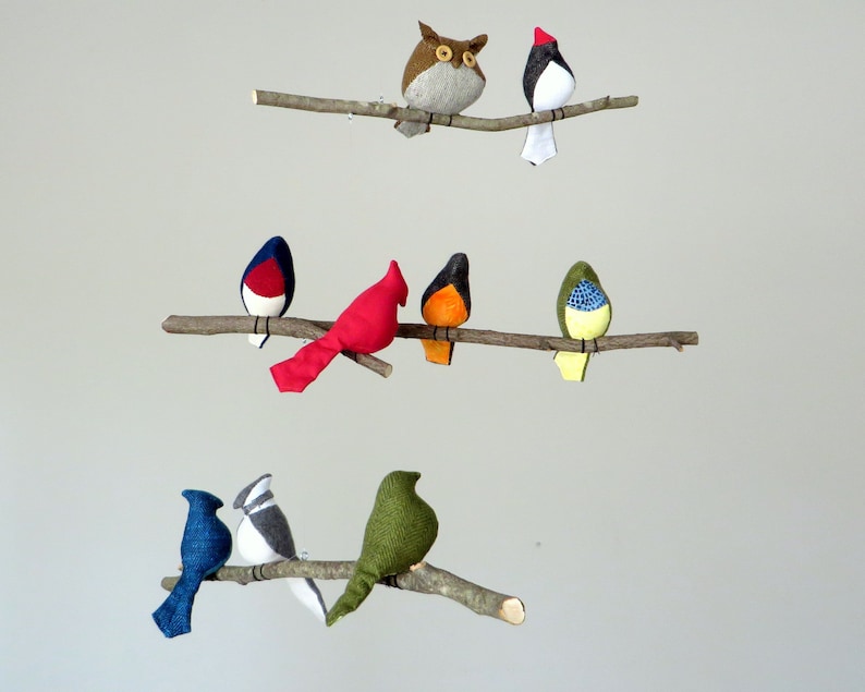 May include: A mobile with seven felt birds hanging from branches. The birds are in various colors, including red, blue, green, yellow, brown, and black. The birds are all facing forward and have a simple design.