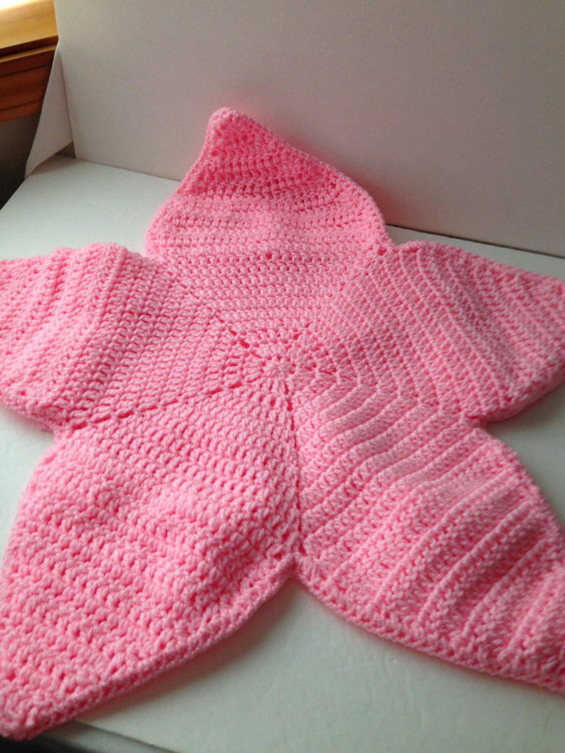 May include: A pink crocheted baby blanket shaped like a star with a pointed hood.