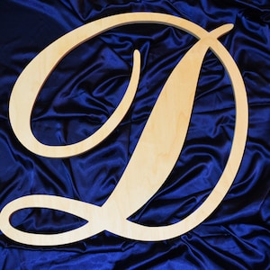 May include: A large, wooden letter D with a cursive script style. The letter is light brown and is displayed against a dark blue background.