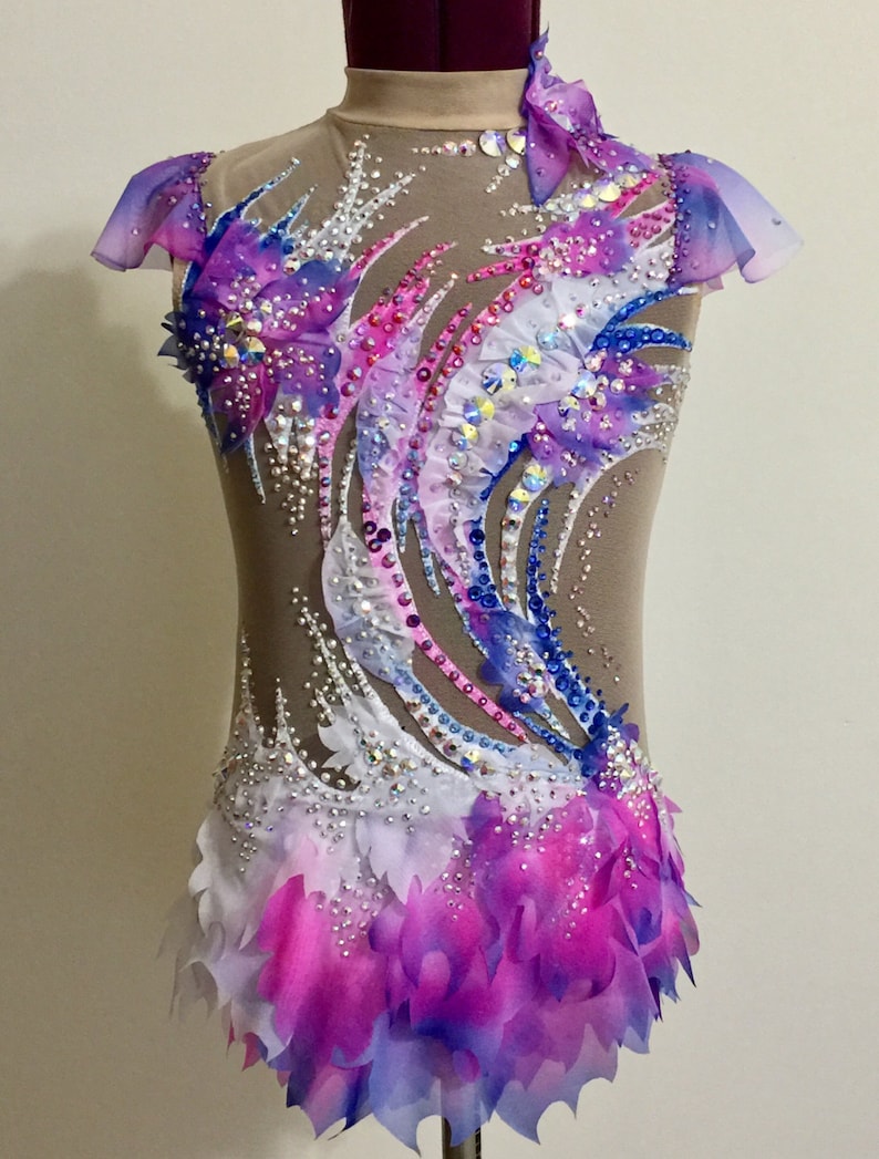 May include: A beige leotard with a high neck and sheer sleeves, adorned with a vibrant design of blue, pink, and purple accents. The costume is embellished with sparkling rhinestones and layered fabric, creating a dynamic and elegant look.
