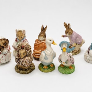 May include: A collection of ceramic figurines featuring various animals. The figurines include a hedgehog, mice, rabbits, and ducks, each with detailed clothing and accessories. The figurines are painted in soft, pastel colors.