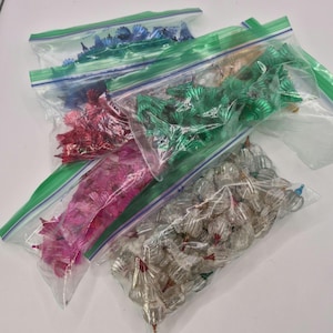 May include: A collection of small, colorful Christmas tree light covers in clear plastic bags. The colors include blue, red, pink, green, and clear. The bags are sealed with green zippers. These are vintage Christmas decorations.