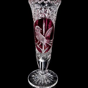 May include: A clear crystal vase with a ruby red interior and a bird design. The vase has a starburst base and a detailed, cut-glass pattern. The bird is etched within an oval shape on the vase.