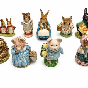 May include: A collection of ceramic figurines depicting various animals in anthropomorphic poses. The figurines include rabbits, mice, a pig, a hedgehog, and a cat, each with detailed clothing and accessories. The color palette is primarily pastel.