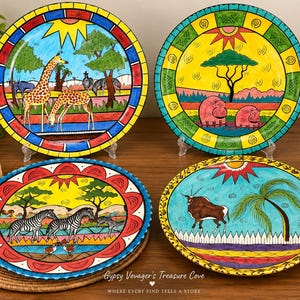 May include: Four round ceramic plates featuring hand-painted African wildlife scenes. One plate shows giraffes, another depicts hippos, a third displays zebras, and the fourth features an antelope. Each plate has a vibrant, colorful border design.