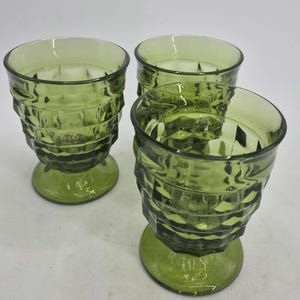 May include: Three green-tinted drinking glasses. Each glass has a faceted, textured design on the body and a rounded base. The glasses are made of a transparent material, allowing light to pass through. The glasses are suitable for serving beverages.