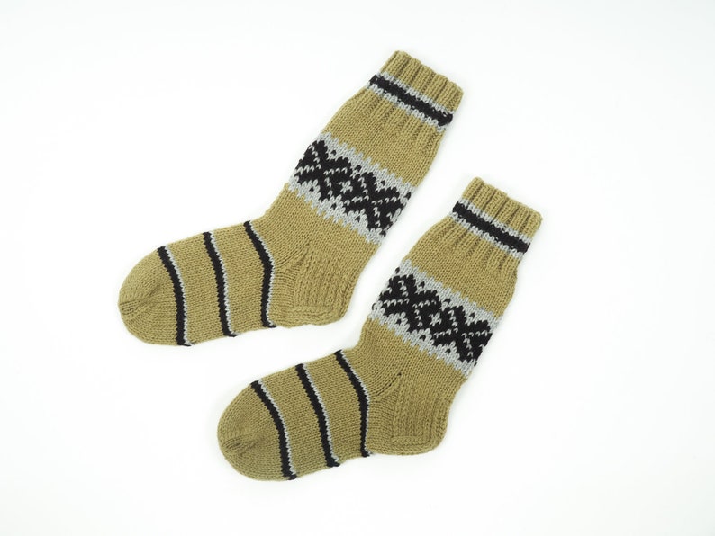 May include: A pair of beige wool socks with black and grey geometric patterns. The socks are knitted and have a ribbed texture.