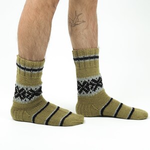 May include: A pair of olive green socks with black and gray stripes and a geometric pattern. The socks are made of a soft, knitted fabric.