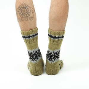 May include: A pair of tan wool socks with black and grey geometric patterns. The socks have a black band around the top.
