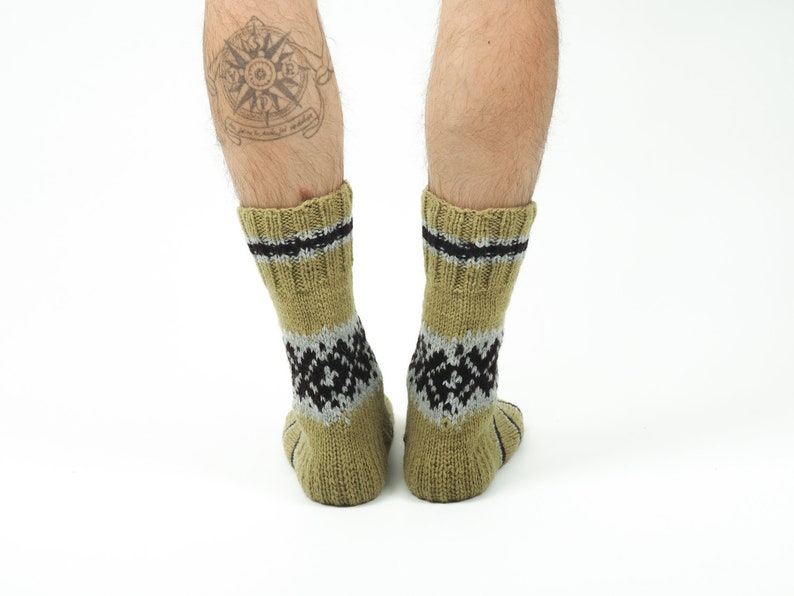 May include: A pair of tan wool socks with black and grey geometric patterns. The socks have a black band around the top.