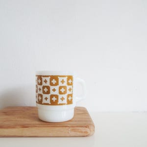 Op de afbeelding: Een witte keramische mok met een zwart handvat en de tekst "But First, Coffee" in een zwarte, vette letter. De mok staat op een wit oppervlak. De mok is 10 cm hoog.