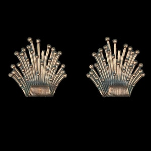 May include: Two silver-toned, fan-shaped earrings. Each earring features a curved base with radiating, thin rods topped with small spheres, creating a textured, ornamental design. The earrings are set against a black background.