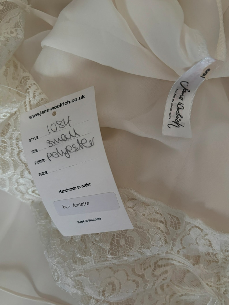 Interior detail view of 2000s y2k vintage new with tags white georgette and lace sheer floor length nightgown with train by Jane Woolrich, size extra small to small. Showing the Jane Woolrich label and paper tag.