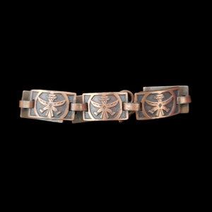 May include: A copper bracelet with three rectangular links, each featuring an embossed design of a stylized bird with outstretched wings.
