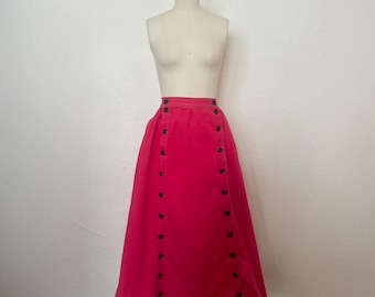 May include: A bright pink skirt with a button-up design. The skirt is displayed on a mannequin and features dark buttons running down the front. The skirt appears to be made of a sturdy fabric and has a classic, A-line shape.