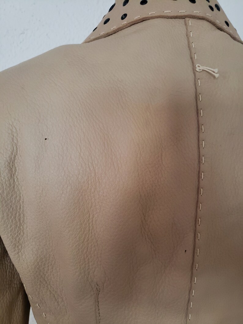 Detail back view of 1990s topstitched metal eyelet and stud embellished buff leather blazer by Donald Pliner, extra small to small, showing the topstitched center back seam and small spots on the jacket.