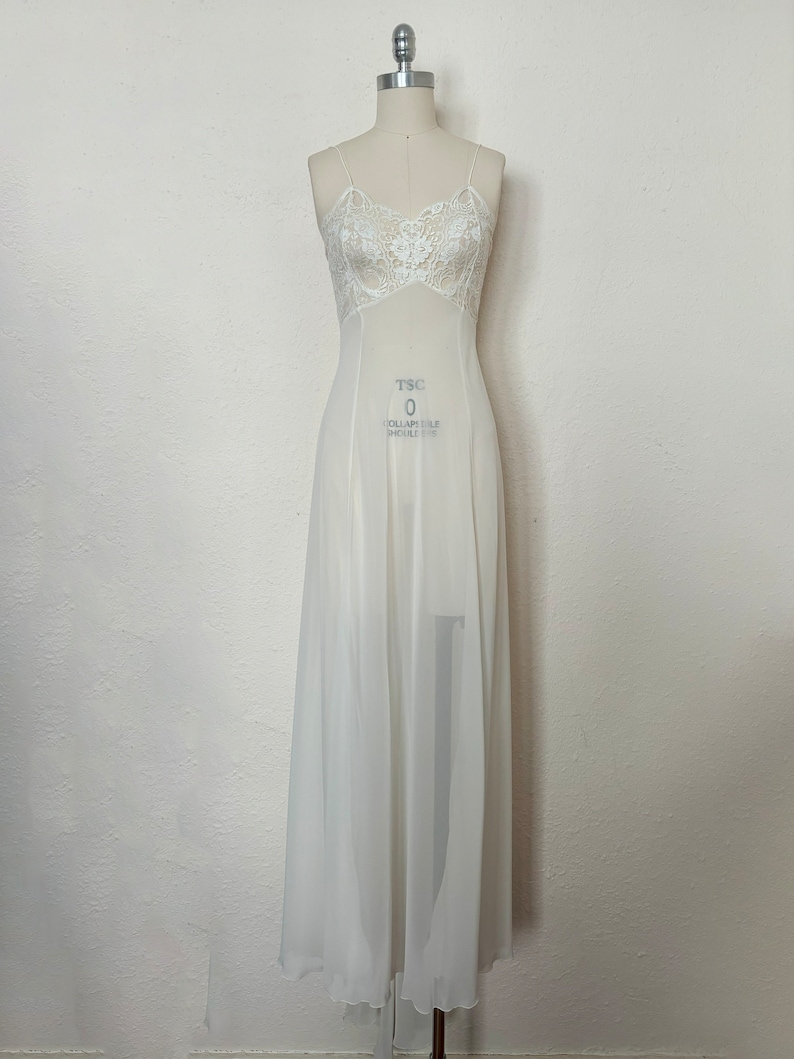 Puede incluir: Un vestido blanco de sat&eacute;n, largo hasta el suelo, con un corpi&ntilde;o de encaje. El vestido tiene tirantes finos y un dobladillo festoneado. El vestido est&aacute; en un maniqu&iacute; blanco.
