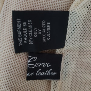 Detail view of 1990s topstitched metal eyelet and stud embellished buff leather blazer by Donald Pliner, extra small to small, showing the mesh lining and fabric content tags.