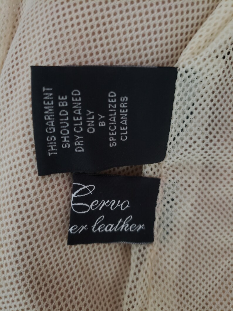 Detail view of 1990s topstitched metal eyelet and stud embellished buff leather blazer by Donald Pliner, extra small to small, showing the mesh lining and fabric content tags.