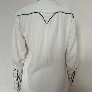 Back view of 1960s vintage white rayon pearl snap western shirt  with navy trim and multicolored embroidery by H bar C, size small to medium.