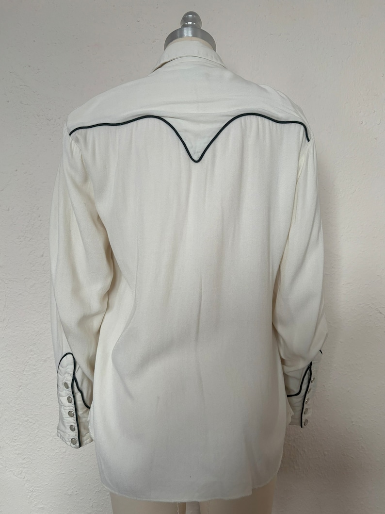 Back view of 1960s vintage white rayon pearl snap western shirt  with navy trim and multicolored embroidery by H bar C, size small to medium.