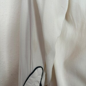 Detail view of 1960s vintage white rayon pearl snap western shirt  with navy trim and multicolored embroidery by H bar C, size small to medium. Showing a spot near the elbow.