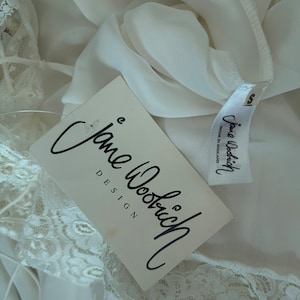 Interior detail view of 2000s y2k vintage new with tags white georgette and lace sheer floor length nightgown with train by Jane Woolrich, size extra small to small. Showing the Jane Woolrich label and paper tag.