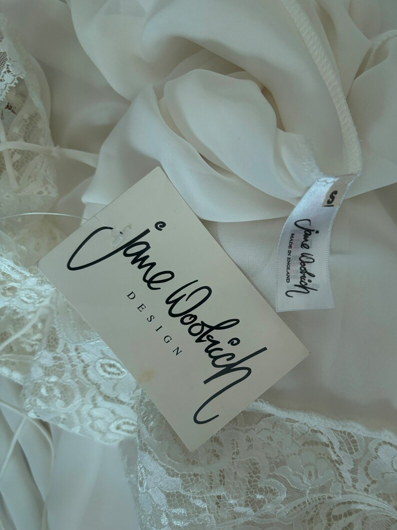 Interior detail view of 2000s y2k vintage new with tags white georgette and lace sheer floor length nightgown with train by Jane Woolrich, size extra small to small. Showing the Jane Woolrich label and paper tag.