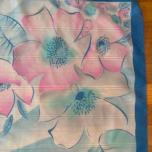 Detail view of 1980s vintage large pink, blue, and white floral print square sheer striped polyester scarf. Showing a close-up of the blue and pink floral print and the snags in the polyester.