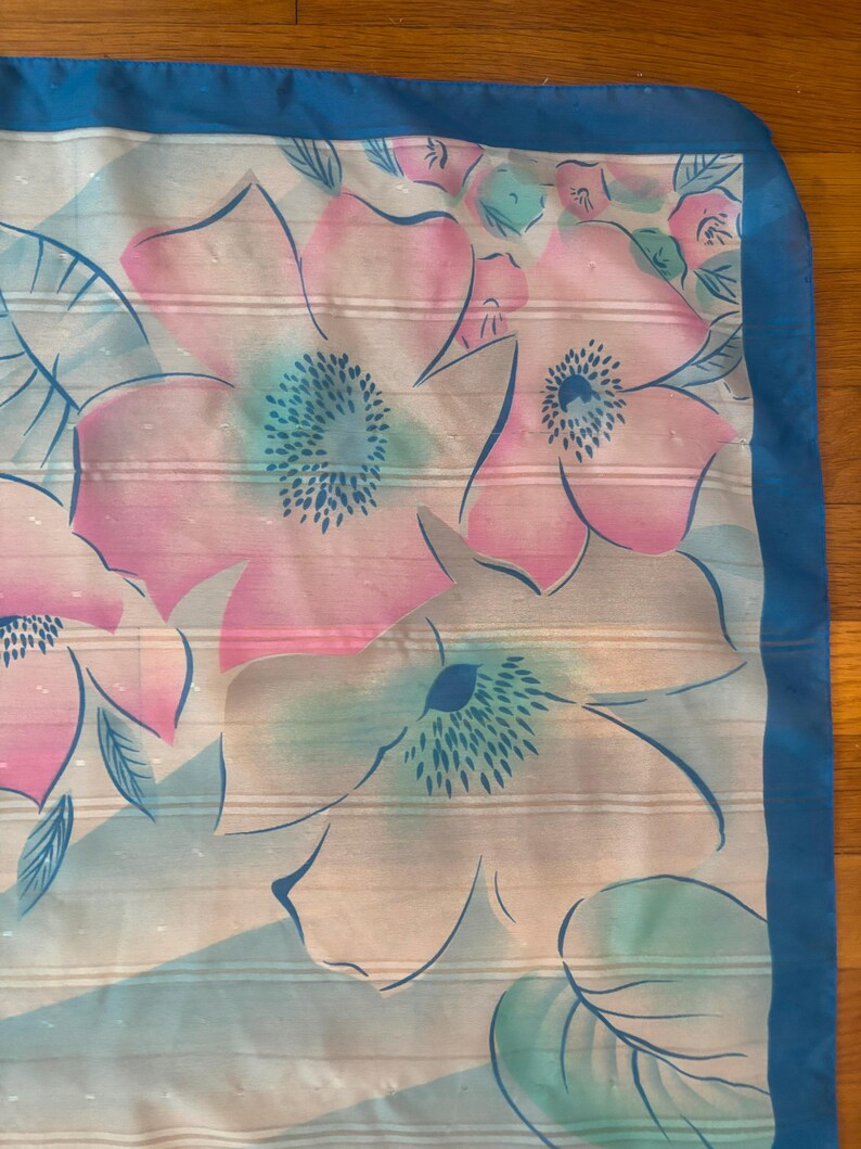 Detail view of 1980s vintage large pink, blue, and white floral print square sheer striped polyester scarf. Showing a close-up of the blue and pink floral print and the snags in the polyester.