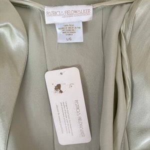 Interior detail view of 2000s y2k vintage new with tags sage green silk charmeuse robe by Patricia Fieldwalker, size medium to large. Showing the Patricia Fieldwalker label, size and paper store tags.