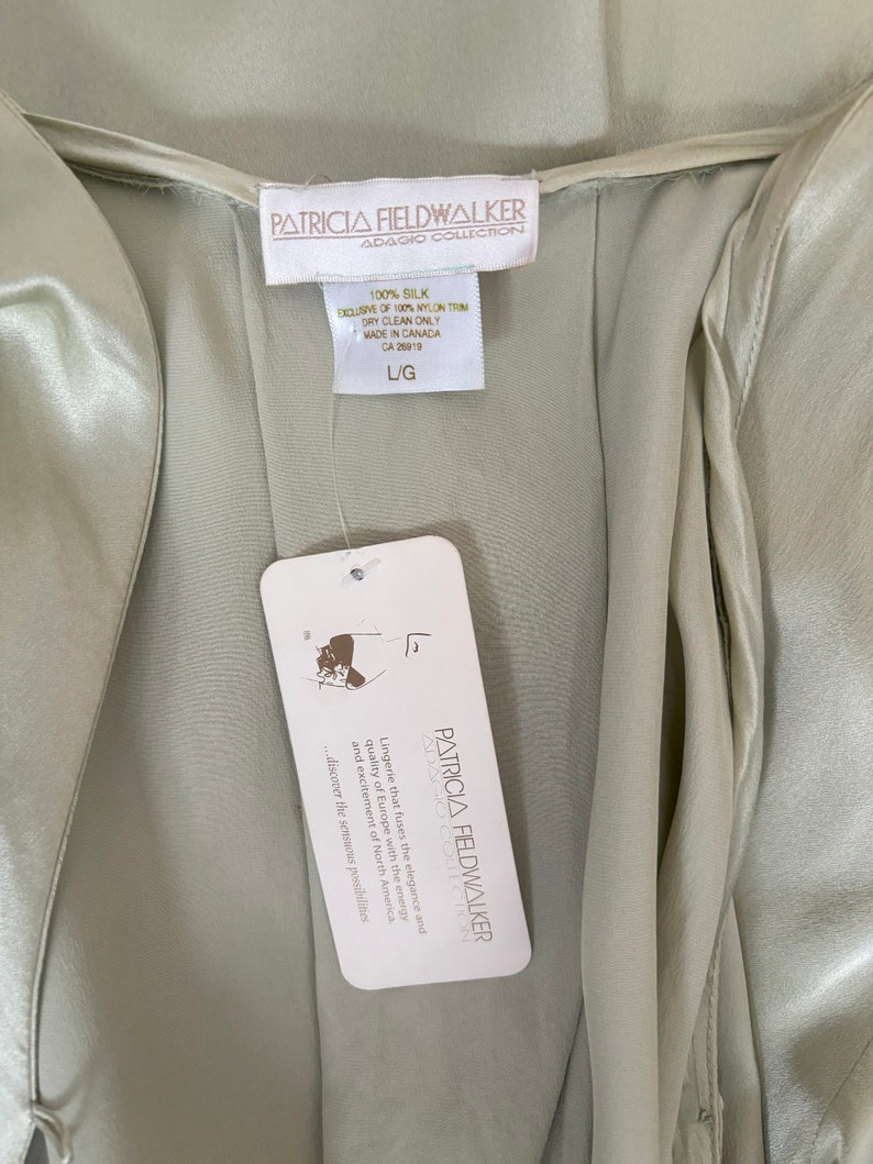 Interior detail view of 2000s y2k vintage new with tags sage green silk charmeuse robe by Patricia Fieldwalker, size medium to large. Showing the Patricia Fieldwalker label, size and paper store tags.