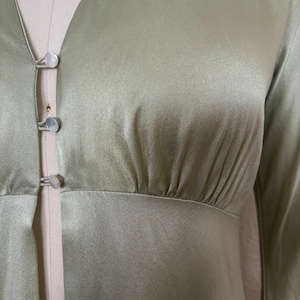Detail view of 2000s y2k vintage new with tags sage green silk charmeuse robe by Patricia Fieldwalker, size medium to large. Showing the gathering under the bust at the empire waist and the mother of pearl buttons.