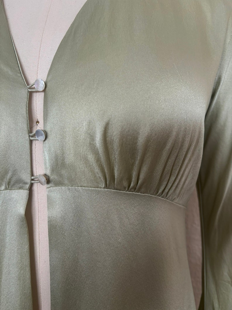 Detail view of 2000s y2k vintage new with tags sage green silk charmeuse robe by Patricia Fieldwalker, size medium to large. Showing the gathering under the bust at the empire waist and the mother of pearl buttons.