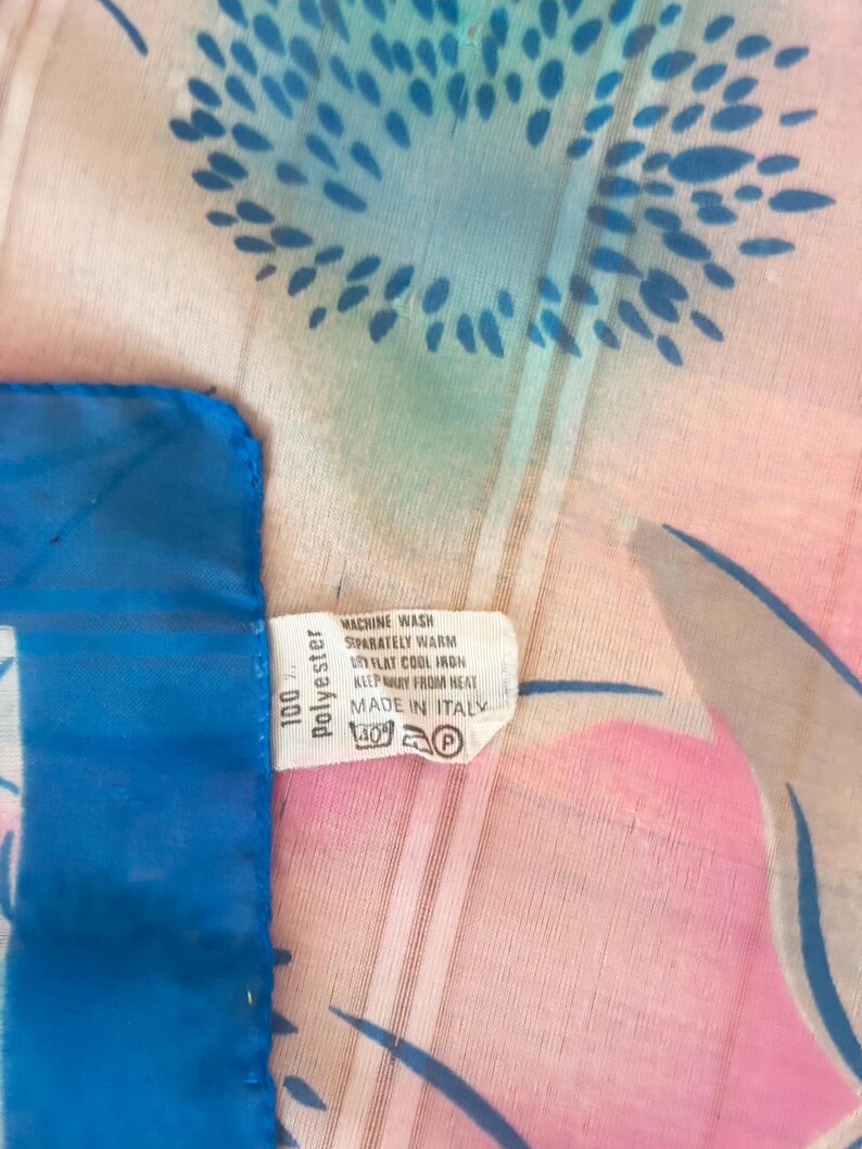 Detail view of 1980s vintage large pink, blue, and white floral print square sheer striped polyester scarf. Showing a close-up of the 100% polyester tag.