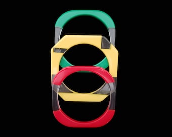 May include: Three square-shaped bangles in red, yellow, and green, stacked vertically against a black background. Each bangle has a clear, rectangular section. The bangles are a bold and colorful accessory.