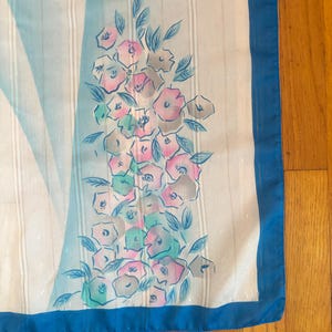 Detail view of 1980s vintage large pink, blue, and white floral print square sheer striped polyester scarf. Showing a close-up of the blue and pink floral print and the snags in the polyester.
