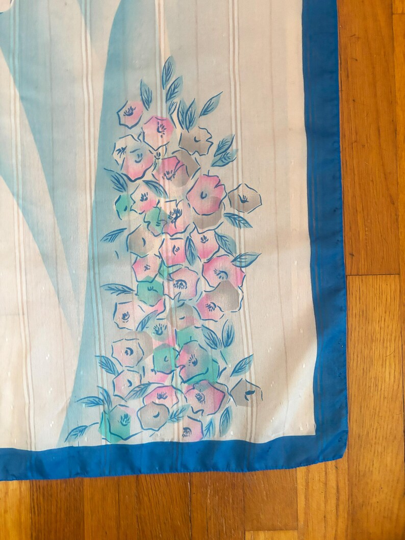 Detail view of 1980s vintage large pink, blue, and white floral print square sheer striped polyester scarf. Showing a close-up of the blue and pink floral print and the snags in the polyester.