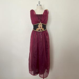May include: A burgundy dress with a sequined bodice and a sheer, flowing skirt. The dress features a black belt with gold and red embellishments. The dress is displayed on a mannequin against a plain background.