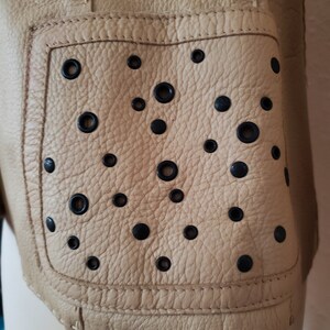 Detail view of 1990s topstitched metal eyelet and stud embellished buff leather blazer by Donald Pliner, extra small to small, showing the patch pockets embellished with black eyelets and studs.