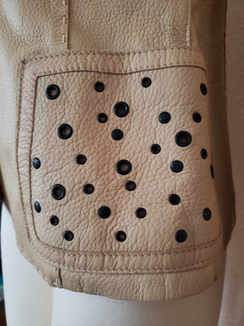 Detail view of 1990s topstitched metal eyelet and stud embellished buff leather blazer by Donald Pliner, extra small to small, showing the patch pockets embellished with black eyelets and studs.