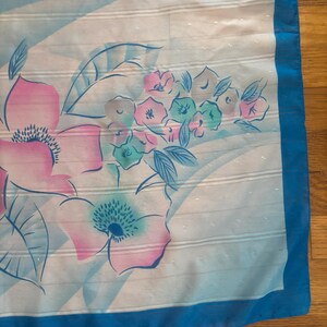 Detail view of 1980s vintage large pink, blue, and white floral print square sheer striped polyester scarf. Showing a close-up of the blue and pink floral print and the snags in the polyester.