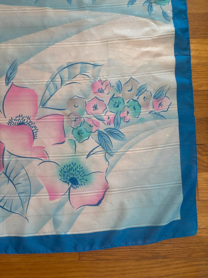 Detail view of 1980s vintage large pink, blue, and white floral print square sheer striped polyester scarf. Showing a close-up of the blue and pink floral print and the snags in the polyester.