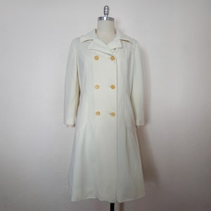 May include: A long, white coat with a double-breasted closure and yellow buttons. The coat has a classic, tailored silhouette.