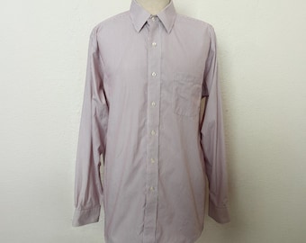 Puede incluir: Una camisa de manga larga con botones y un patrón a rayas en tonos rosa y blanco. La camisa tiene un cuello clásico y un solo bolsillo en el pecho.