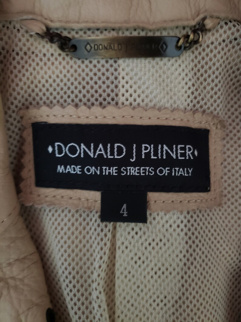 Detail view of 1990s topstitched metal eyelet and stud embellished buff leather blazer by Donald Pliner, extra small to small, showing the tag and label.