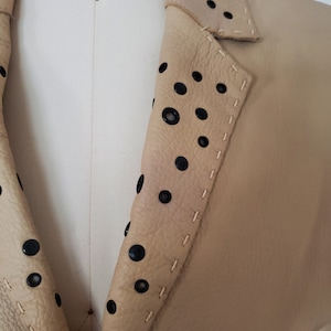 Detail view of 1990s topstitched metal eyelet and stud embellished buff leather blazer by Donald Pliner, extra small to small, showing the topstitched collar embellished with black eyelets and studs.